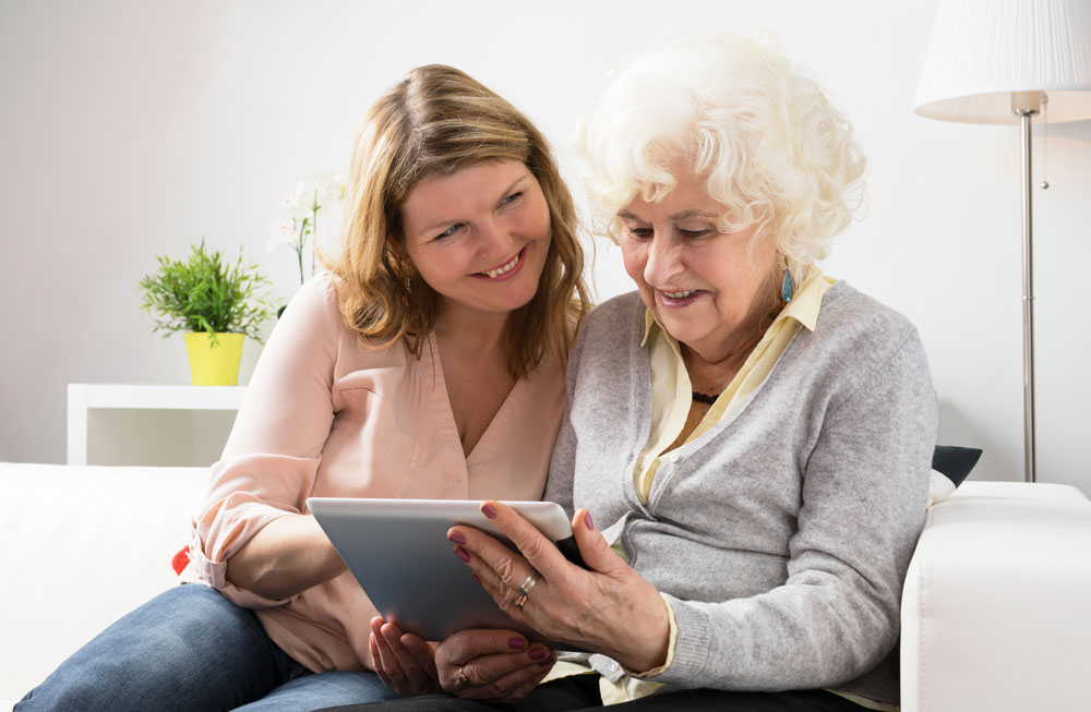 une dame et un senior qui regardent ensemble quelque chose sur une tablette