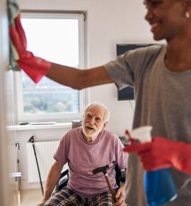 une dame qui nettoie une porte et un monsieur en fauteuil roulant