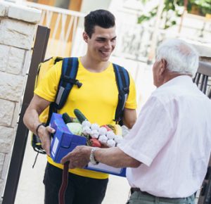 un jeune homme qui livre un panier de courses à un senior